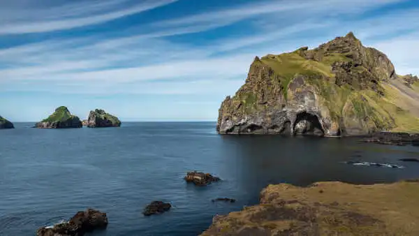 An immense rock, looking exactly like an elephant stands in the ocean under a bright blue sky